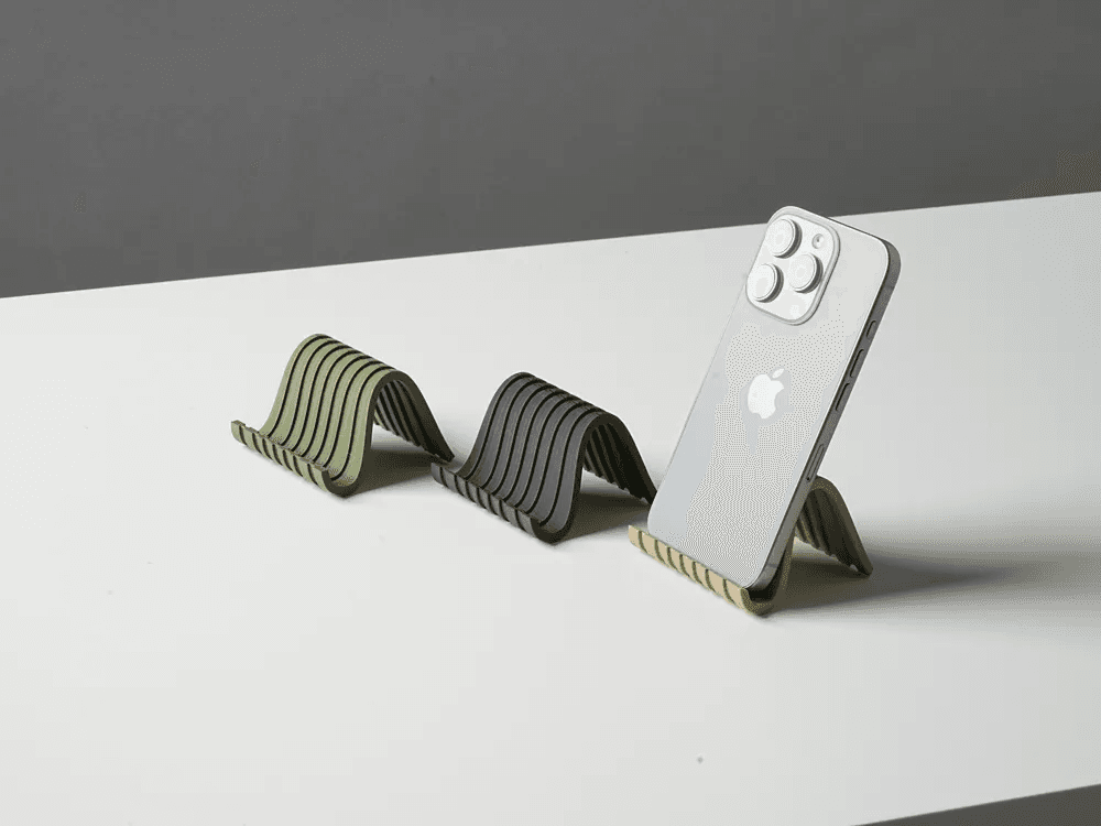 Support de téléphone ondulé, coloris vert, noir et beige, avec un smartphone posé sur le modèle beige